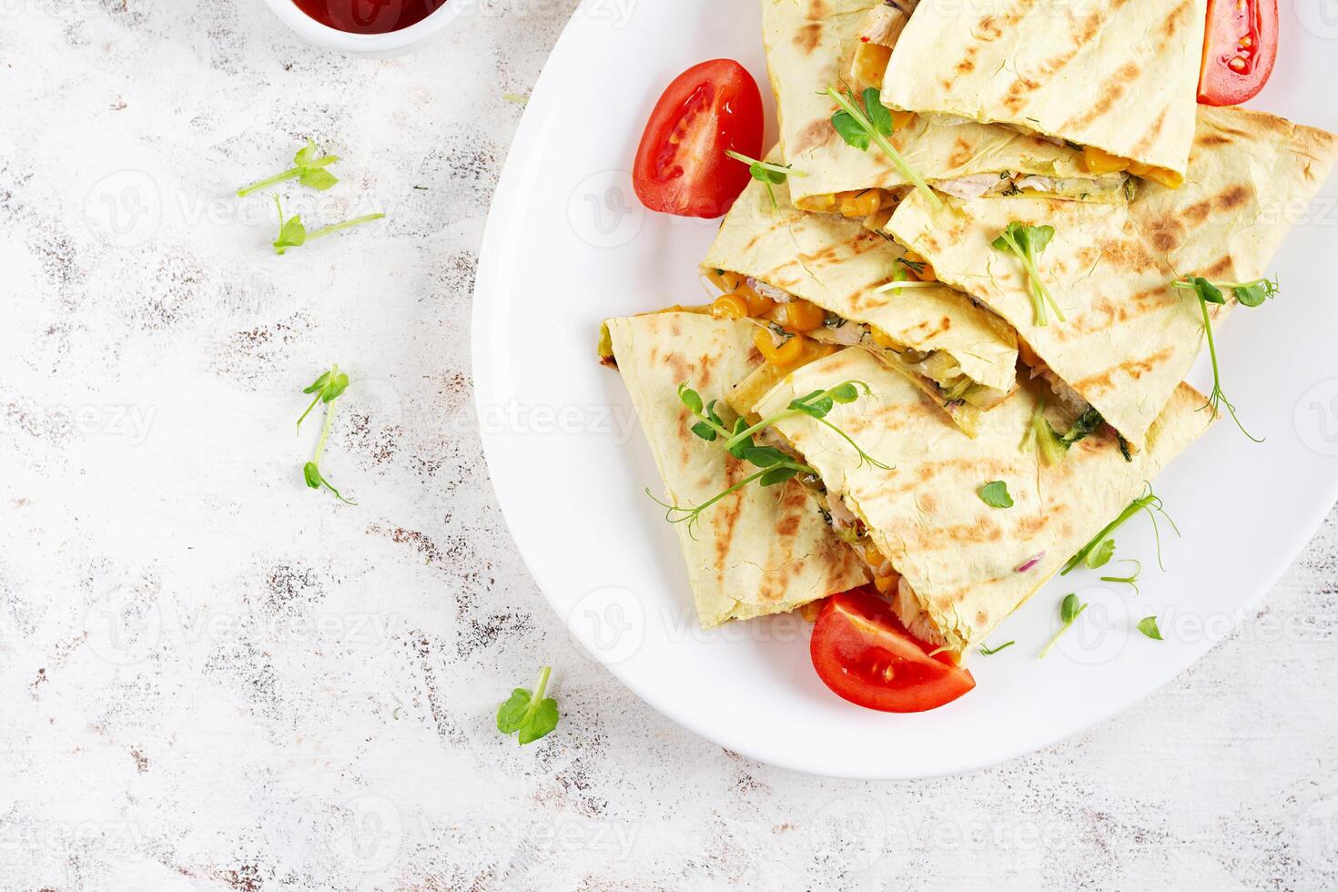 Mexican Quesadilla wrap with chicken, corn and sweet pepper on white plate. Top view photo