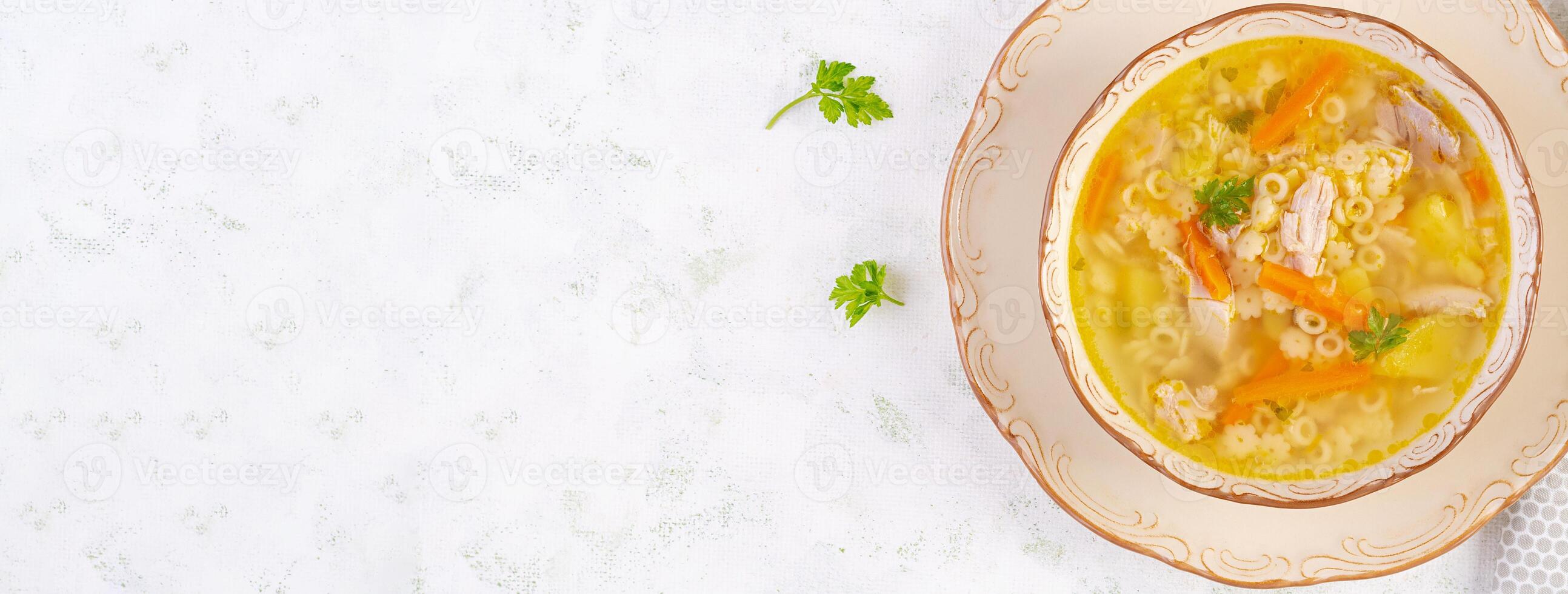 Fresh chicken soup with vegetables and stelline pasta in a bowl with carrot and parsley. Top view, banner photo