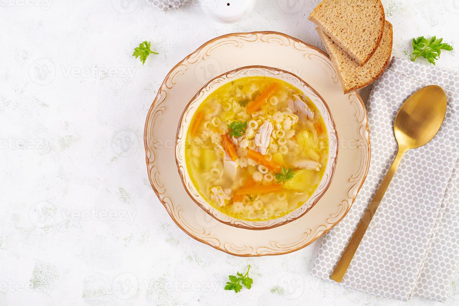 Fresh chicken soup with vegetables and stelline pasta in a bowl with carrot and parsley. Top view, flat lay photo