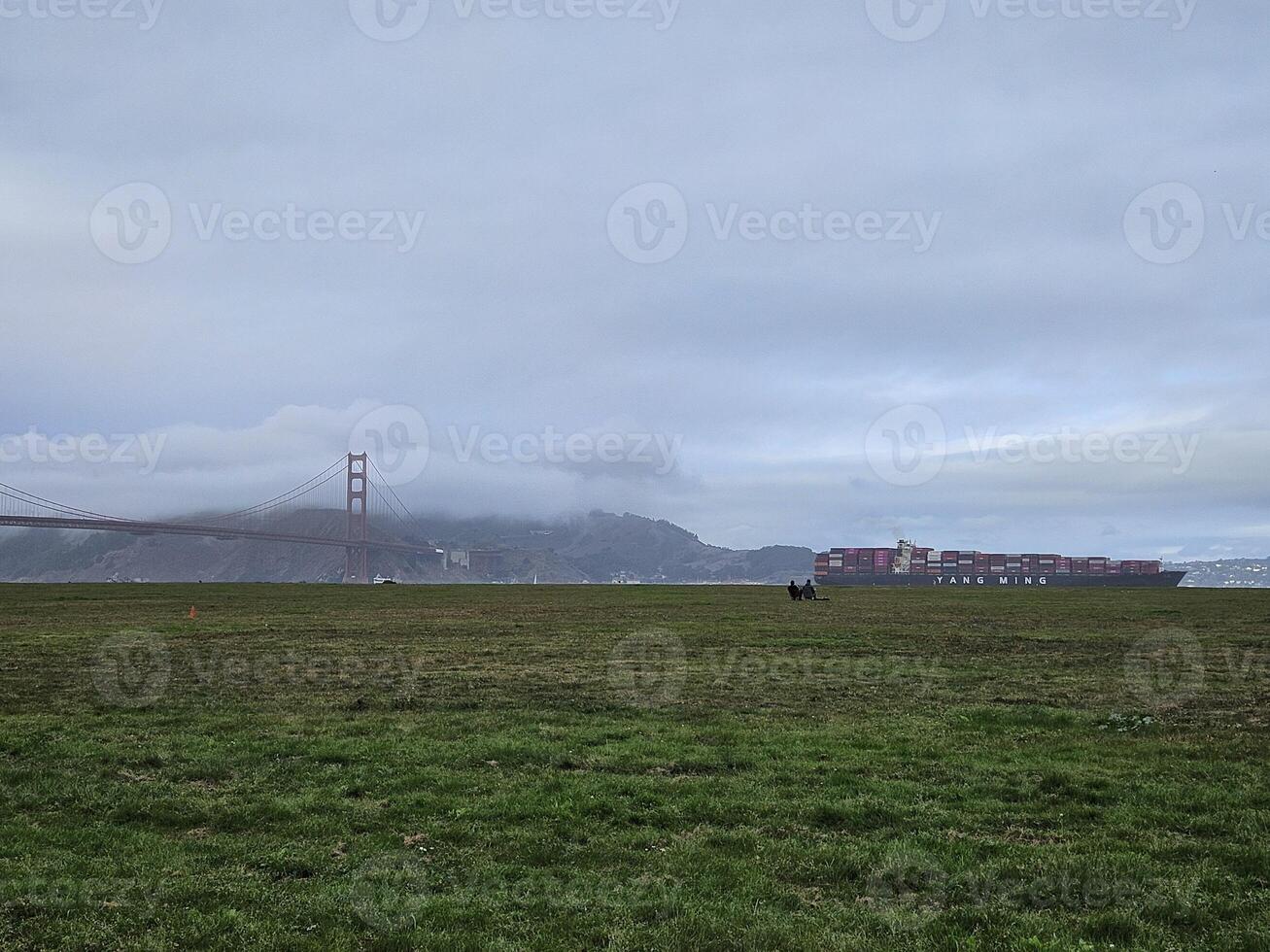 View of Golden Gate Bridge at a foggy day with a container barge passing by photo