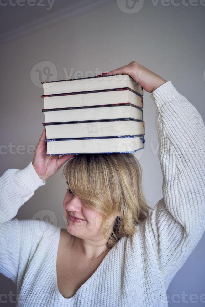 a medium-sized woman in light clothes plays with books in a light room photo