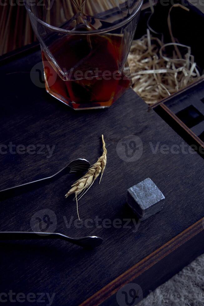 whiskey with tongs, stone cubes, wooden box and wheat on carpet photo