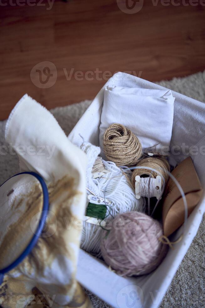 tamaño medio mujer en ligero ropa borda un imagen en oro y beige tonos mientras sentado en un blanco silla en un ligero habitación foto