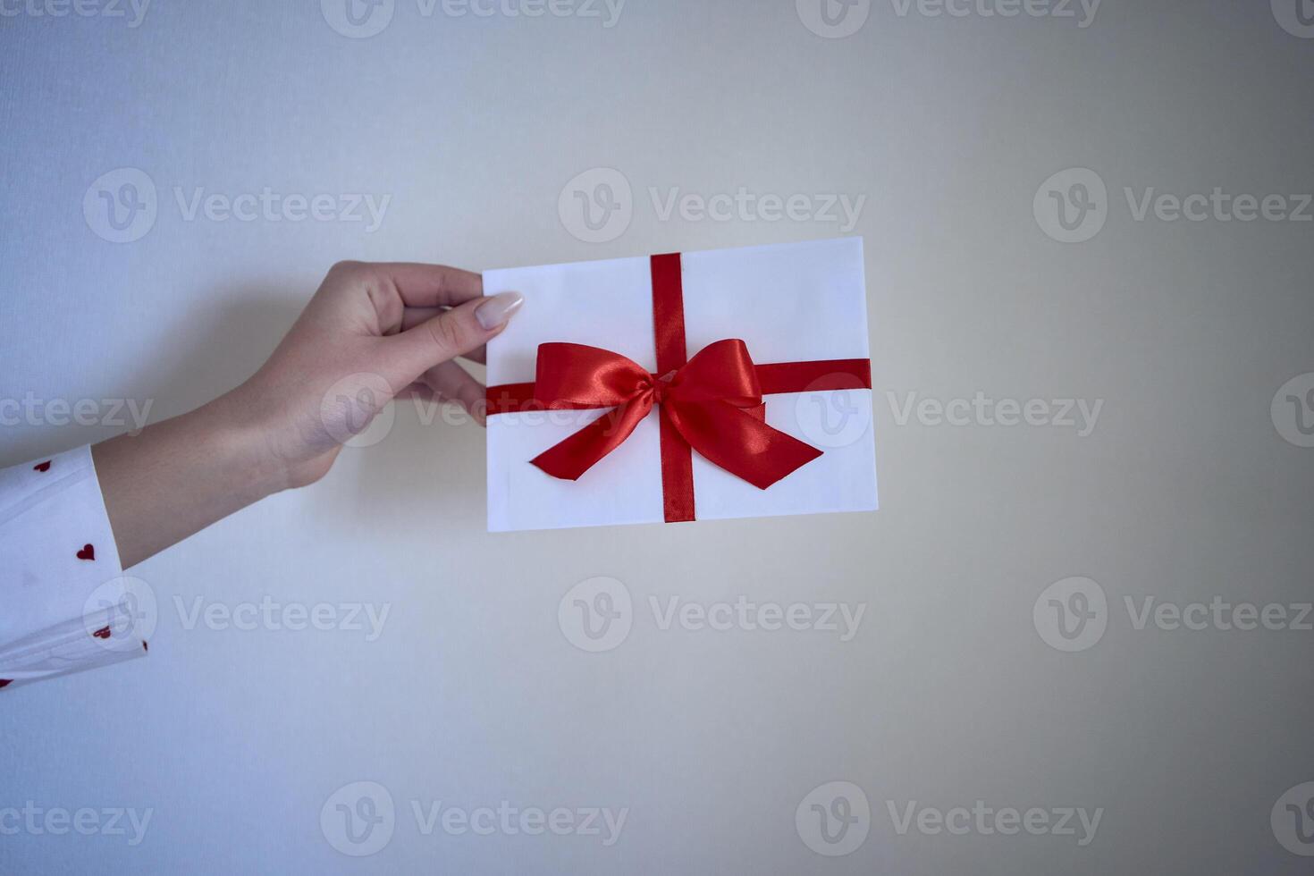 gift certificate in red and white colors in female hands on a white wall background photo