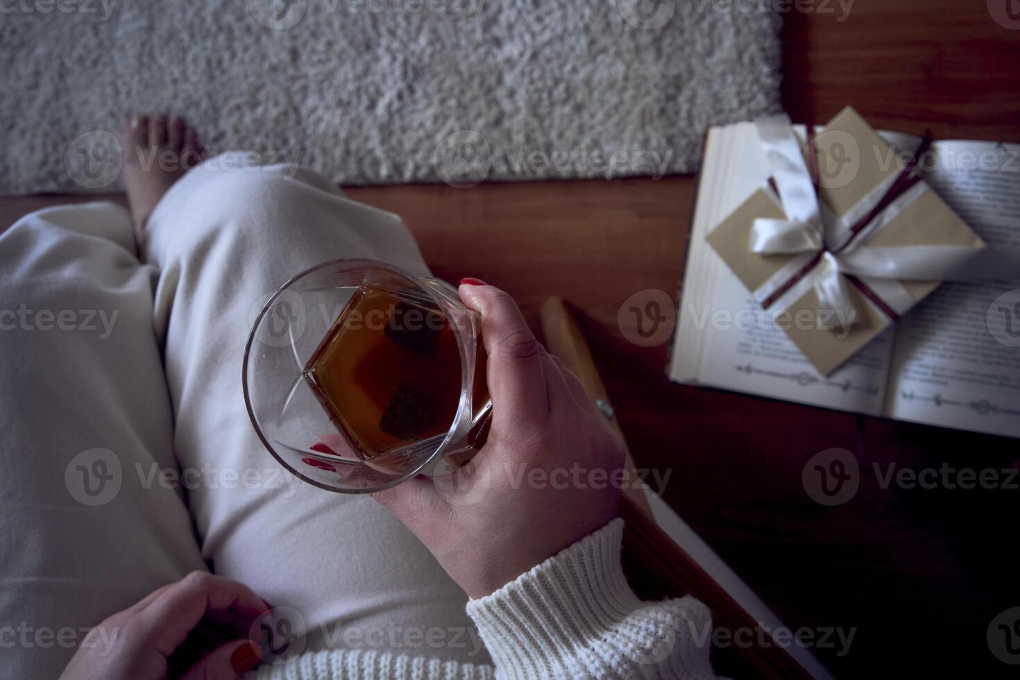 a medium-sized woman sits in an armchair reading a book and drinking whiskey, a gift certificate is next to her photo