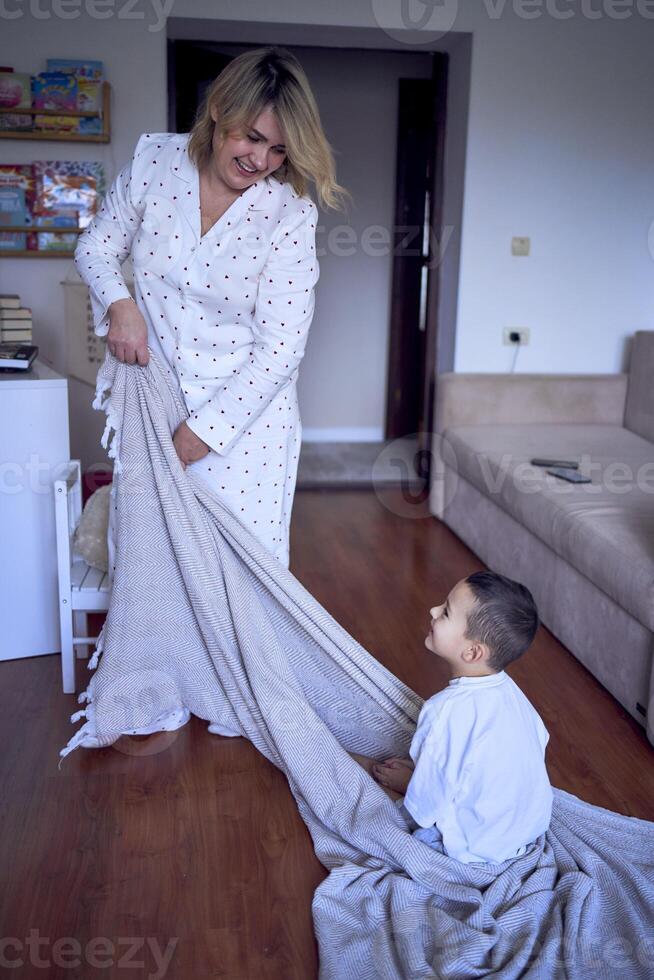 un madre obras de teatro y arrastra su pequeño hijo en un sábana alrededor el habitación foto