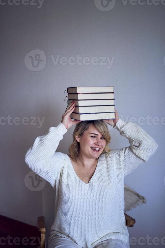 a medium-sized woman in light clothes plays with books in a light room photo