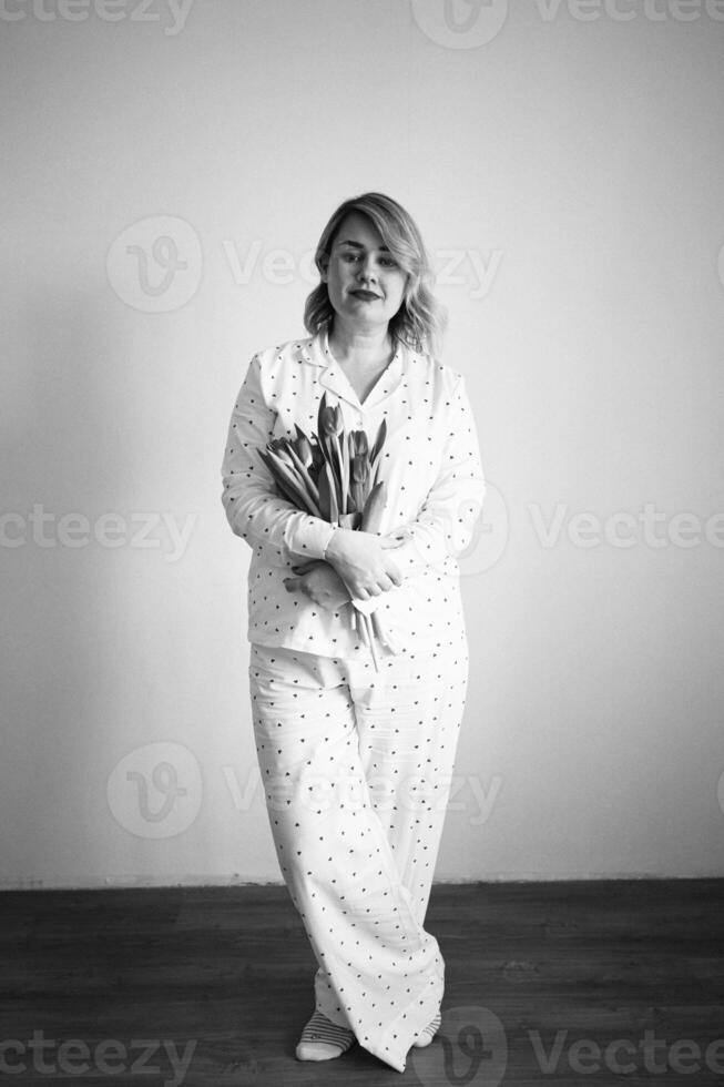 portrait of a beautiful medium-sized woman in pajamas with a bouquet of red tulips in a minimalist style photo