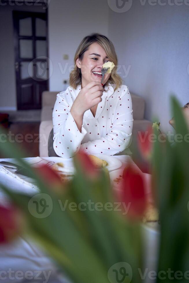 familia de tres, madre, Adolescente hija y pequeño hijo, comiendo pastel en pijama a un mesa con tulipanes foto