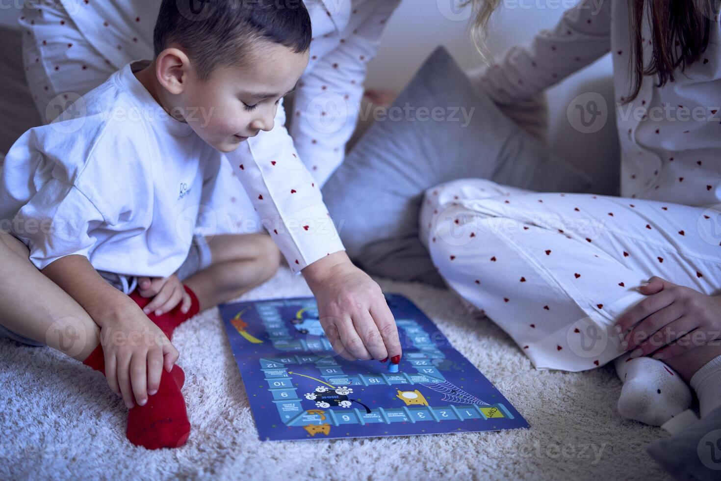 mother with teenage daughter and little son in pajamas playing board games on the floor photo