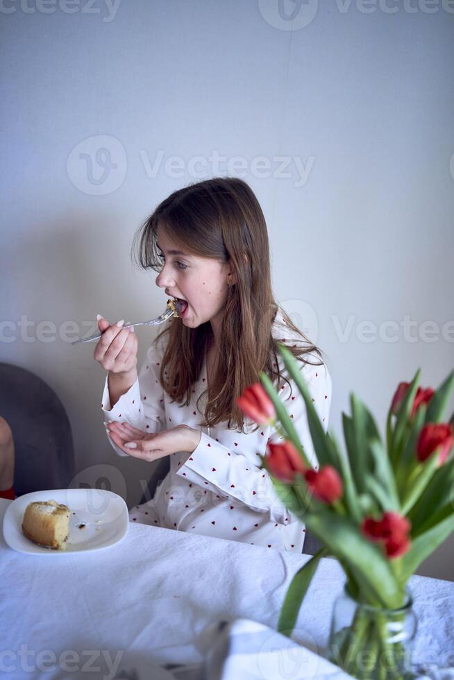 familia de tres, madre, Adolescente hija y pequeño hijo, comiendo pastel en pijama a un mesa con tulipanes foto