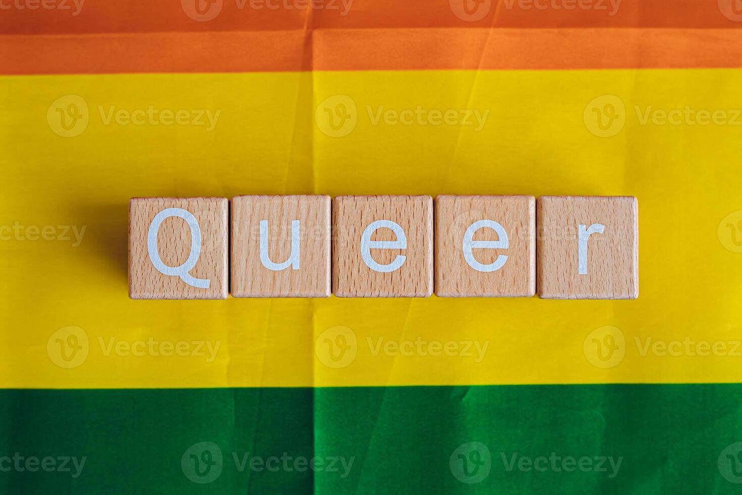 Wooden blocks form the text Queer against a rainbow background. photo