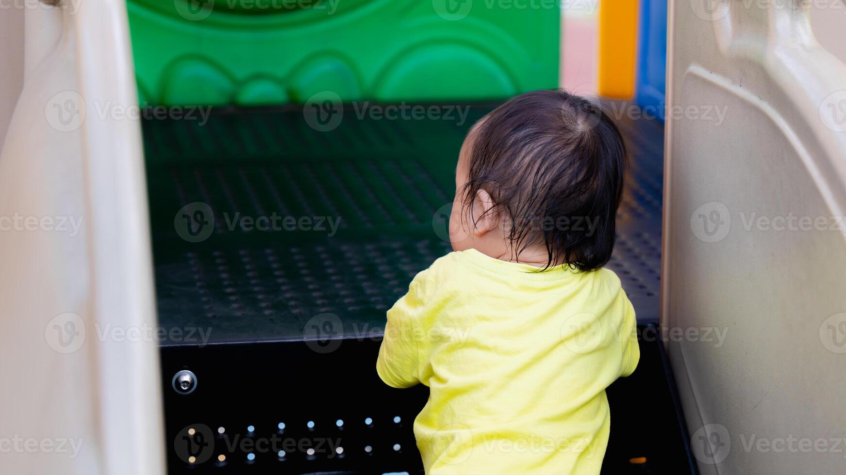 asiático bebé chico es aprendizaje a escalada arriba pasos. niñito es trabajando en bruto motor a el patio de juegos. activo niño es fuera de pisar arriba en equipo también grande para su pequeño cuerpo. niño Envejecido un año de edad. foto