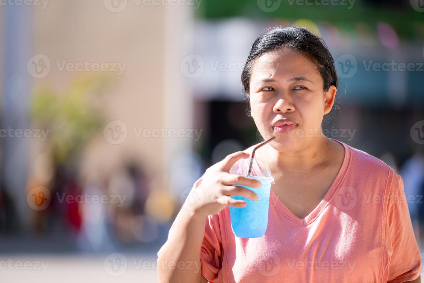 A woman is drinking clear blue soda water in a plastic glass with a straw, on a very hot day, refreshing and thirst-quenching the body. Empty space for entering text. photo