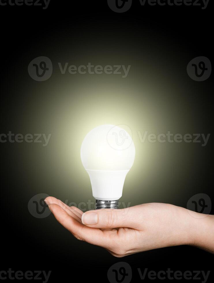 woman's hand holding light bulb on black background photo