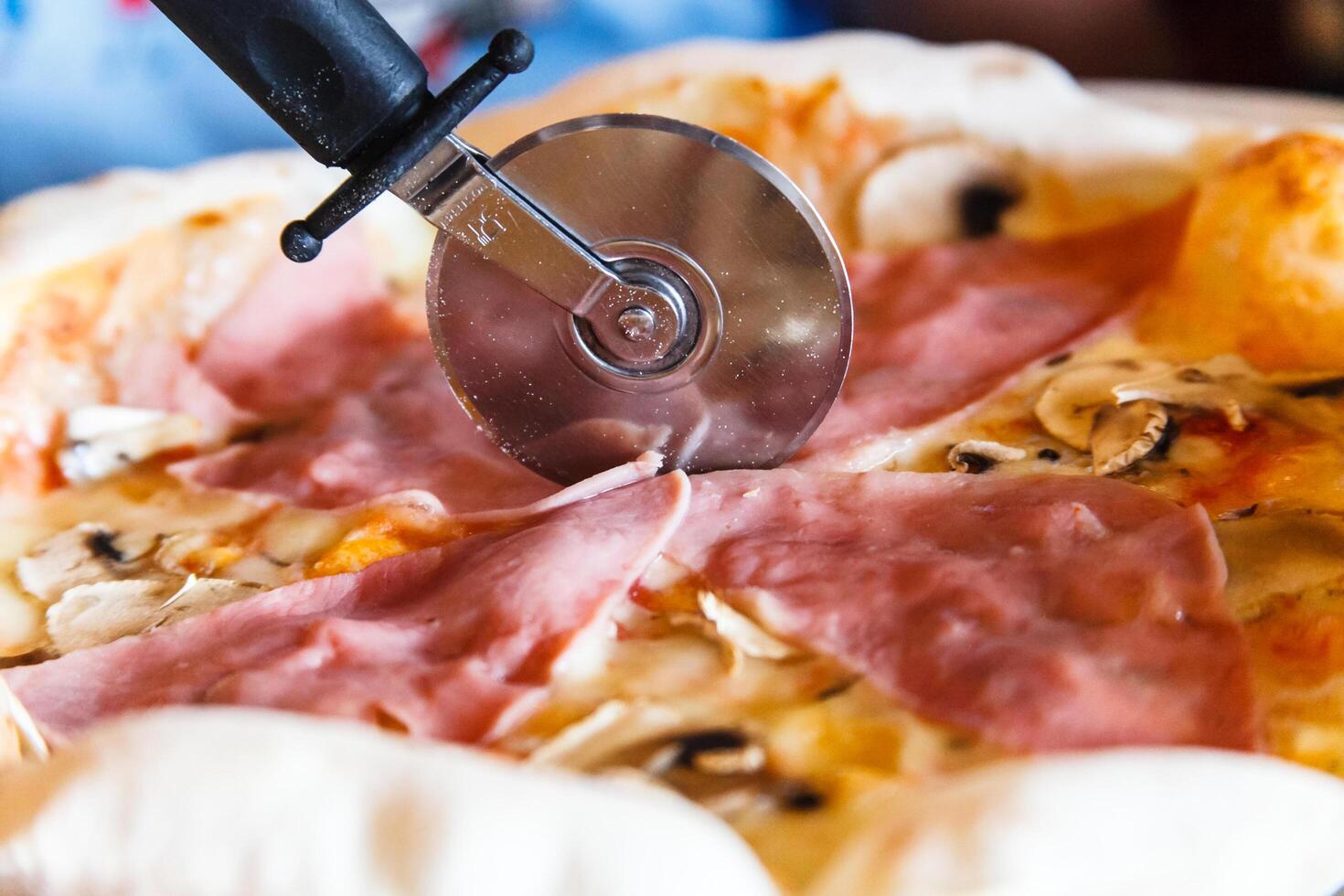 The round knife cuts the pizza with ham. photo