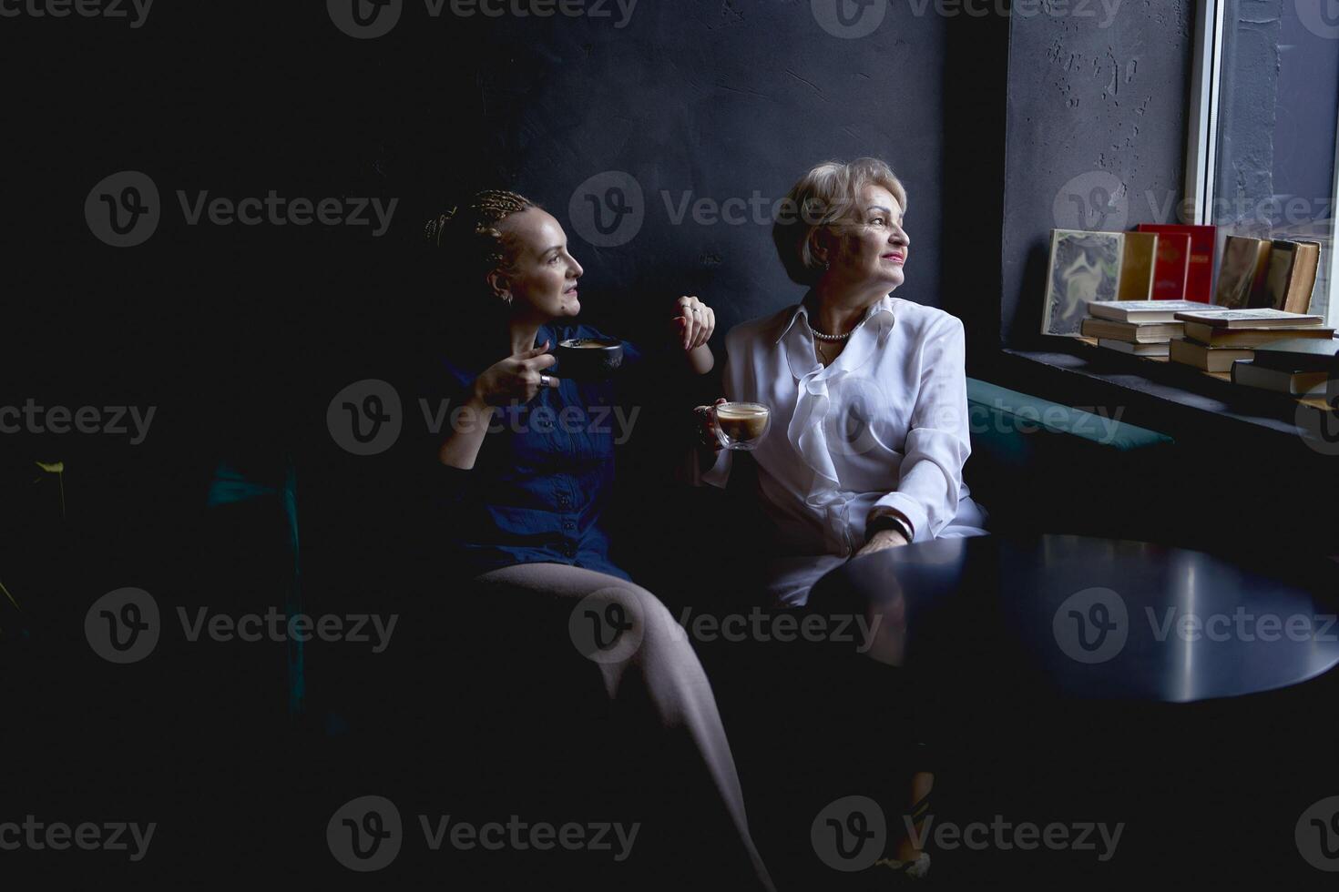 old mother and middle-aged daughter drinking coffee and talking in the cafe photo