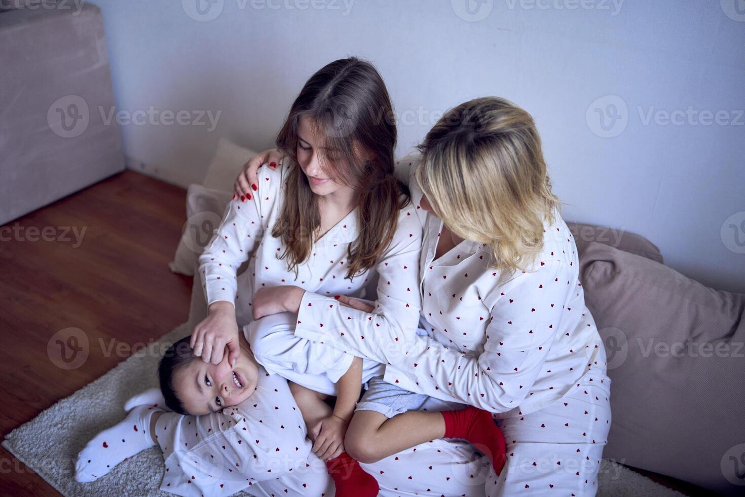 a mother and teenage girl in pajamas tickle younger brother on the floor photo