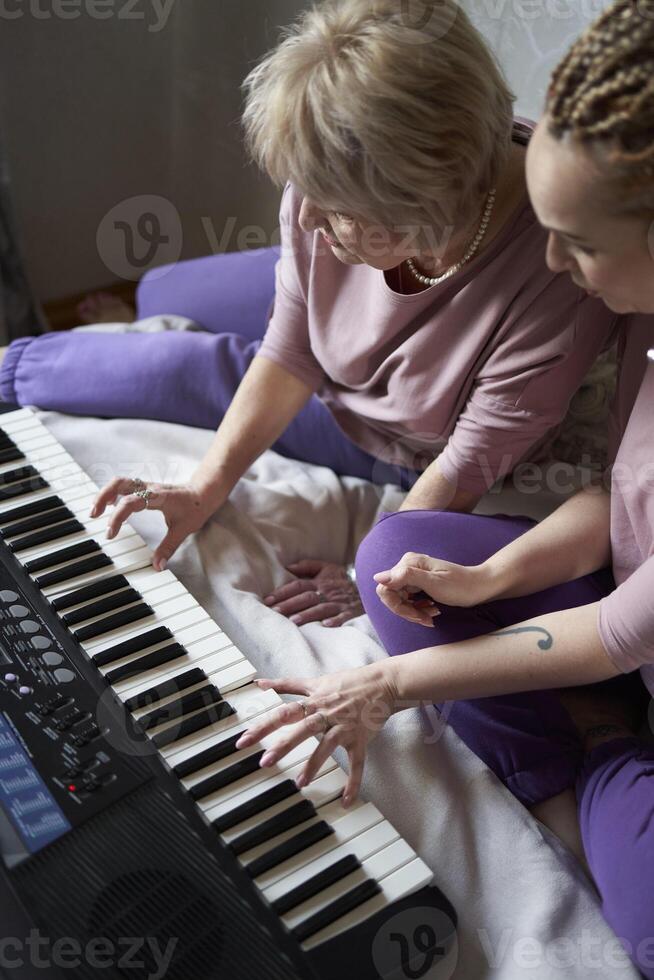 A 60-year-old mother and a 40-year-old daughter play the keyboard together on the bed at home photo