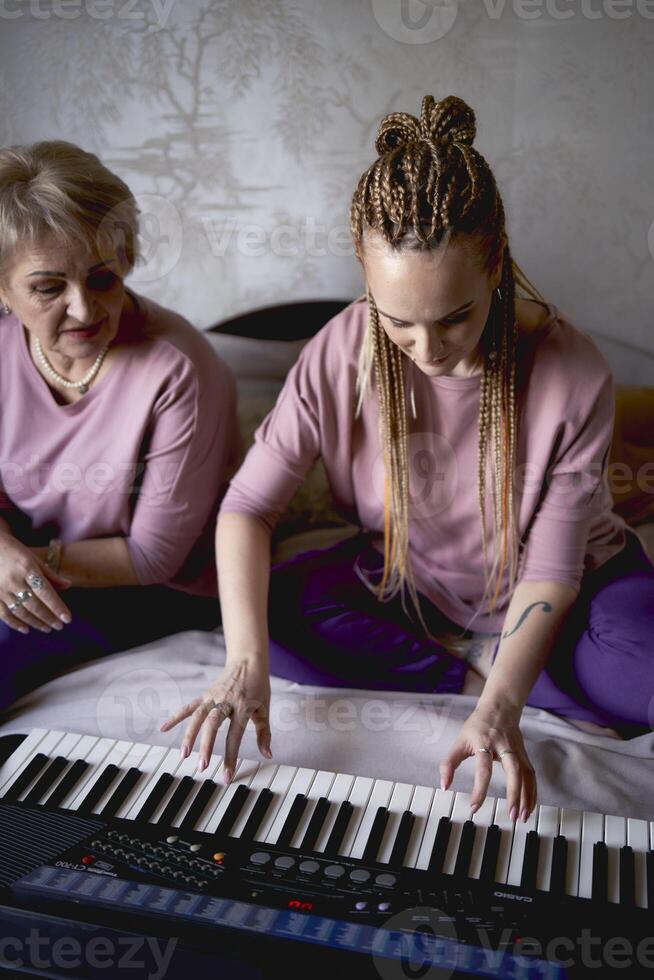 un 60 años madre y un 40 años hija jugar el teclado juntos en el cama a hogar foto