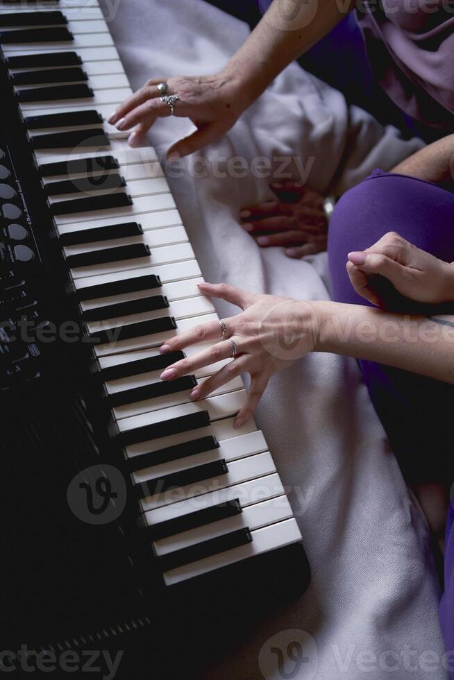 A 60-year-old mother and a 40-year-old daughter play the keyboard together on the bed at home photo