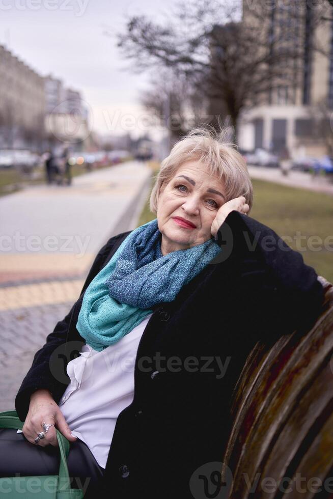 retrato de un elegante antiguo mujer en un negro Saco con verde accesorios en un primavera calle foto