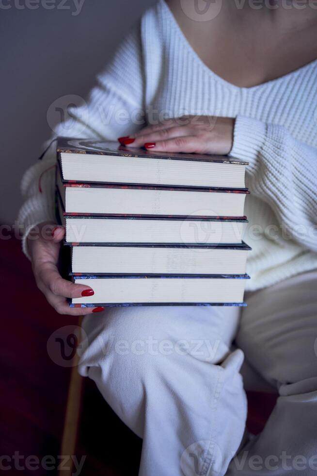 un talla media mujer en ligero ropa lee un libro mientras sentado en un blanco silla en un ligero habitación foto