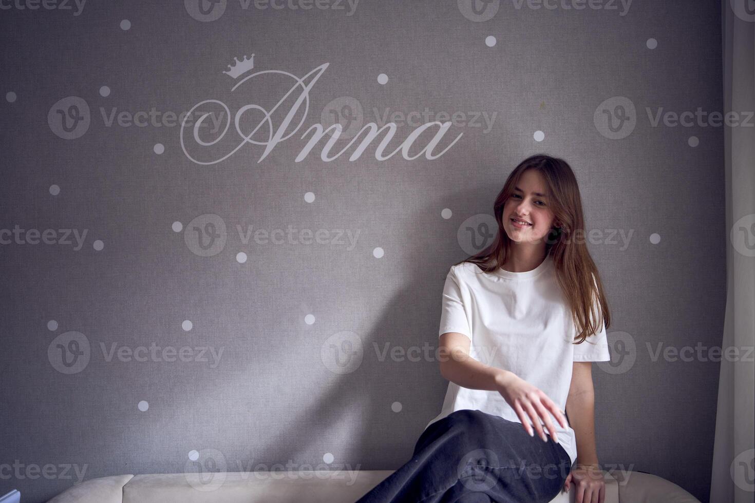 a beautiful teenage girl sits on a bed near the wall with her name written on it photo