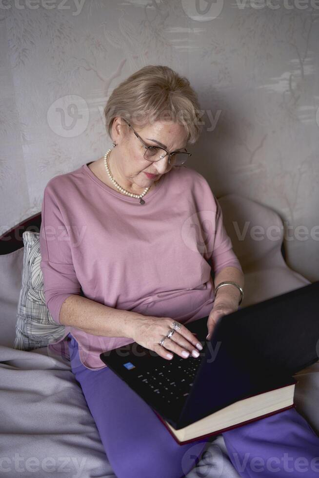 un mayor mujer trabajos con ordenador portátil a hogar foto