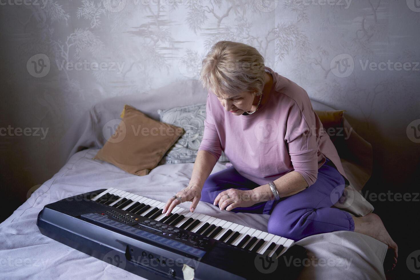 A 60-year-old mother and a 40-year-old daughter play the keyboard together on the bed at home photo