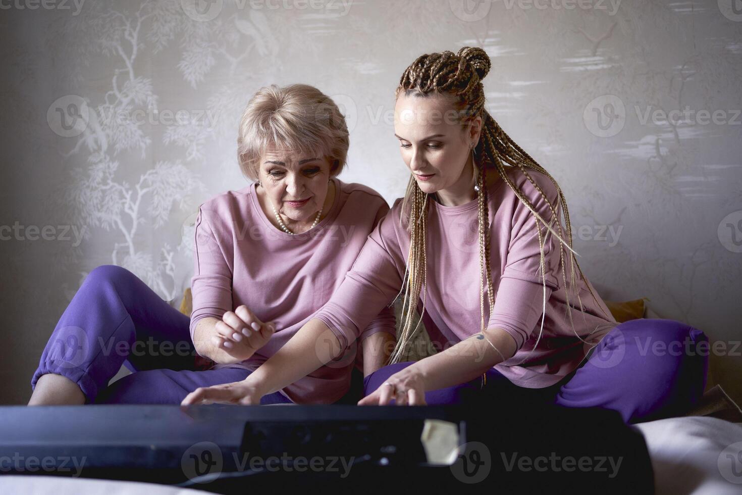 A 60-year-old mother and a 40-year-old daughter play the keyboard together on the bed at home photo