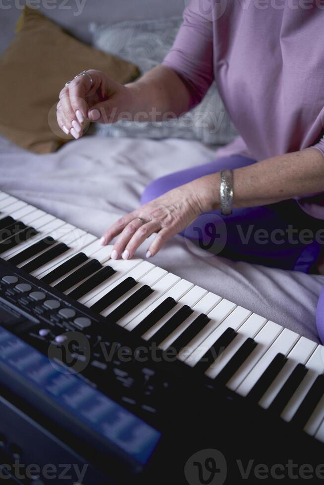 A 60-year-old mother and a 40-year-old daughter play the keyboard together on the bed at home photo