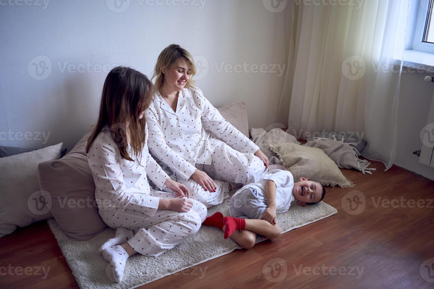 a mother and teenage girl in pajamas tickle younger brother on the floor photo