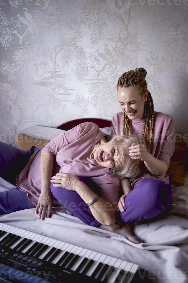 A 60-year-old mother and a 40-year-old daughter play the keyboard together on the bed at home photo