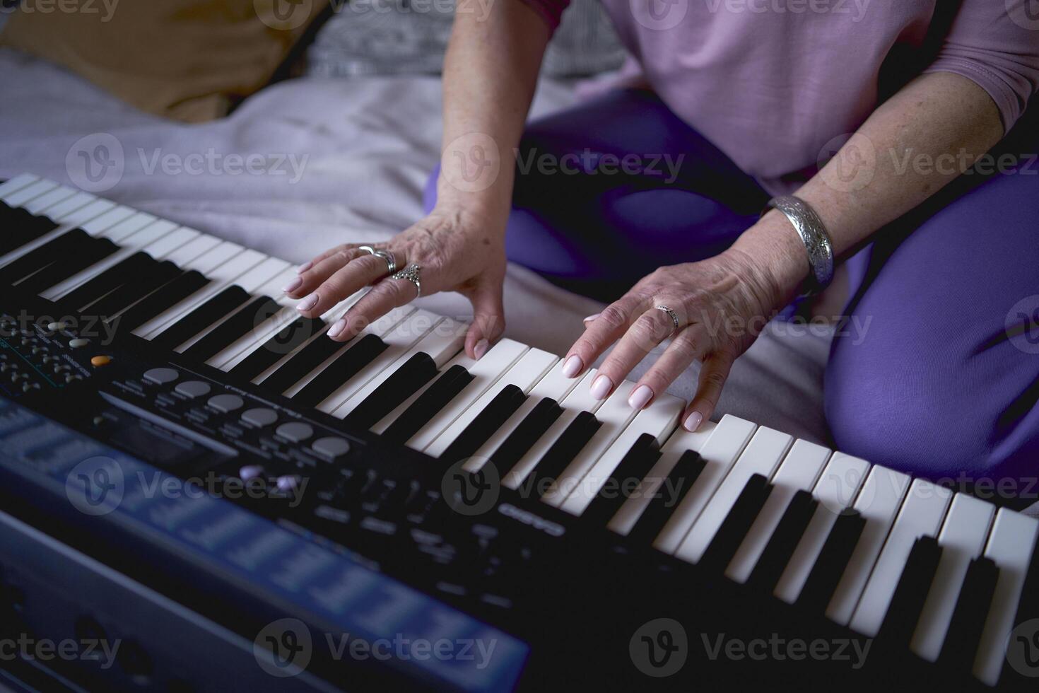 A 60-year-old mother and a 40-year-old daughter play the keyboard together on the bed at home photo