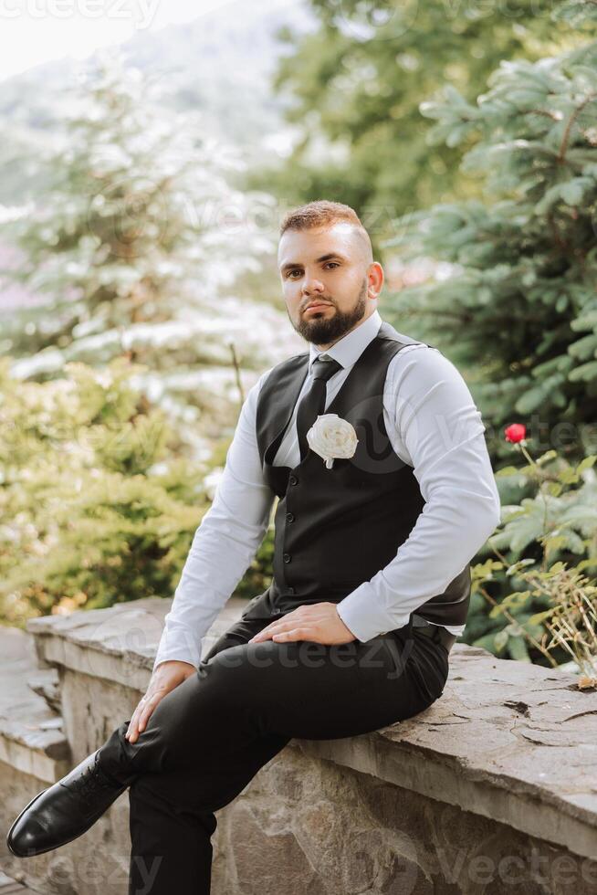 Portrait of the groom in nature in the summer. Stylish tall groom in an elegant black business suit. Businessman in nature. Portrait of a successful man. Wedding portrait of the groom. photo