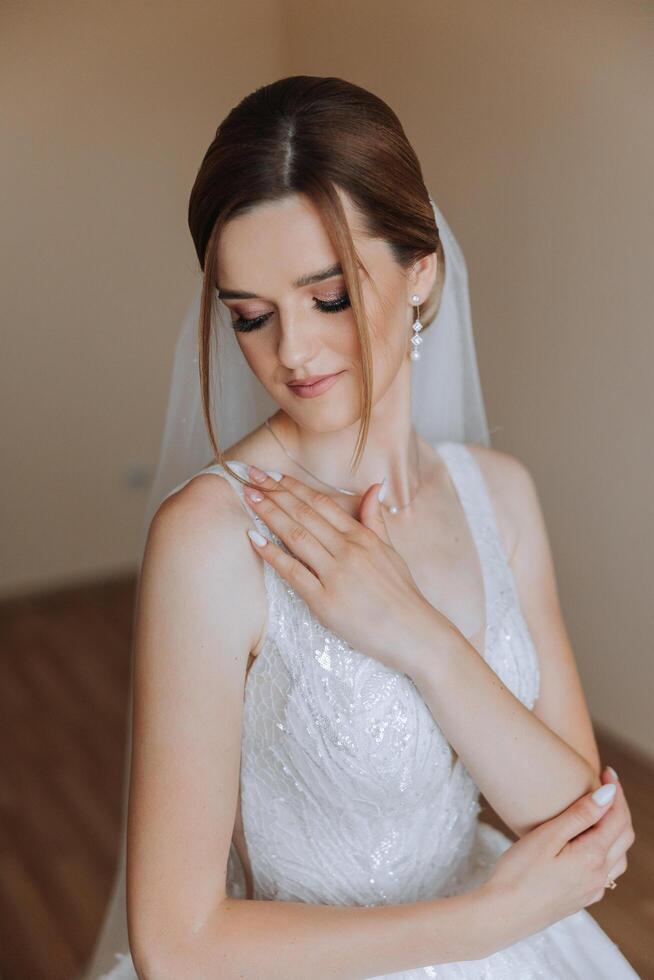 Portrait of the bride in the hotel room. A beautiful young girl is dressed in a white wedding dress. Modern wedding hairstyle. Natural makeup. photo