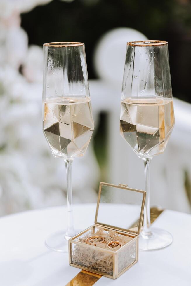 conformado champán lentes y un vaso caja con oro Boda anillos en el medio. preparación para el Boda ceremonia. foto