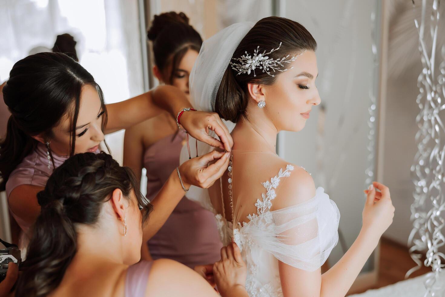 Wedding morning. Bridesmaids help put on the white wedding dress. A young woman is preparing to meet her groom and having fun with her friends photo
