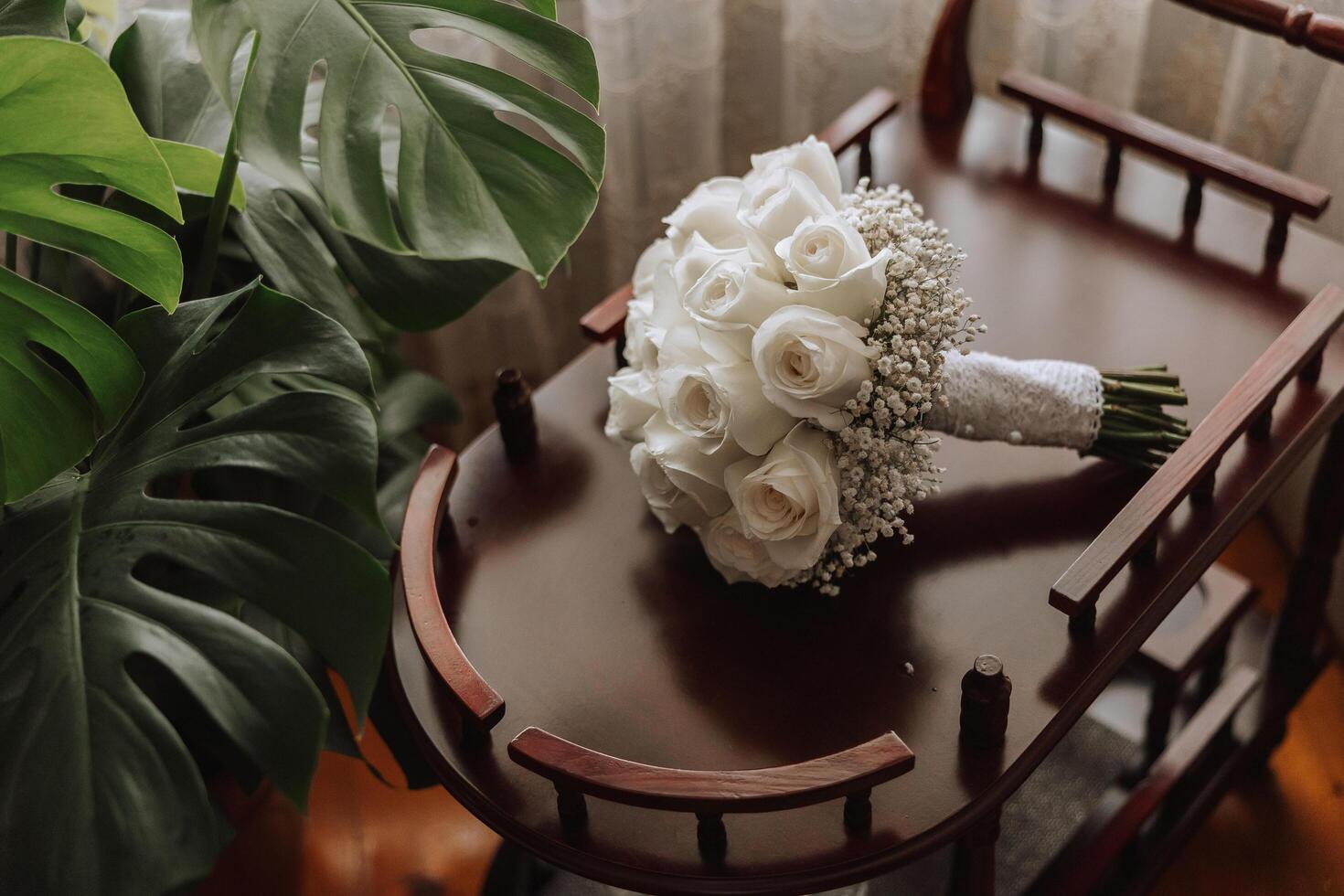 Wedding bouquet. White cut roses, green seed heads and leaves. Green stems and white ribbon and gold wedding rings. photo