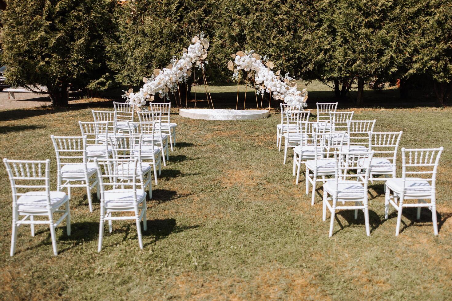 Decorative modern wedding arch made of white flowers in nature. Many white chairs for the wedding ceremony. Everything is ready for the celebration. photo