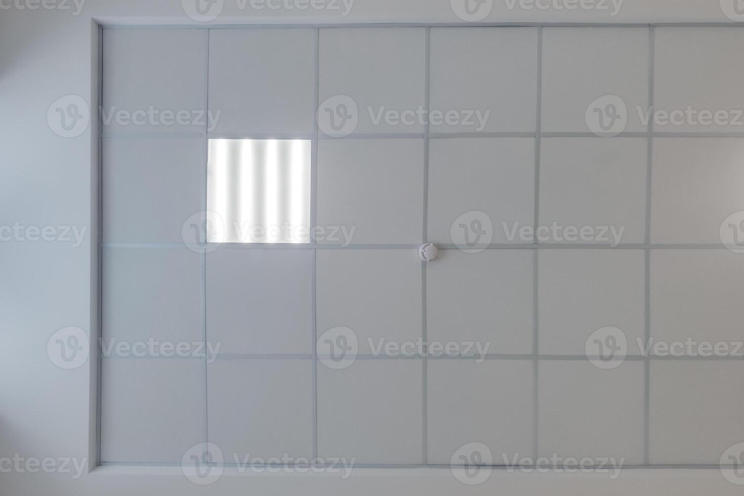 cassette stretched or suspended ceiling with square halogen spots lamps and drywall construction in empty room in house or office with column. Looking up view photo