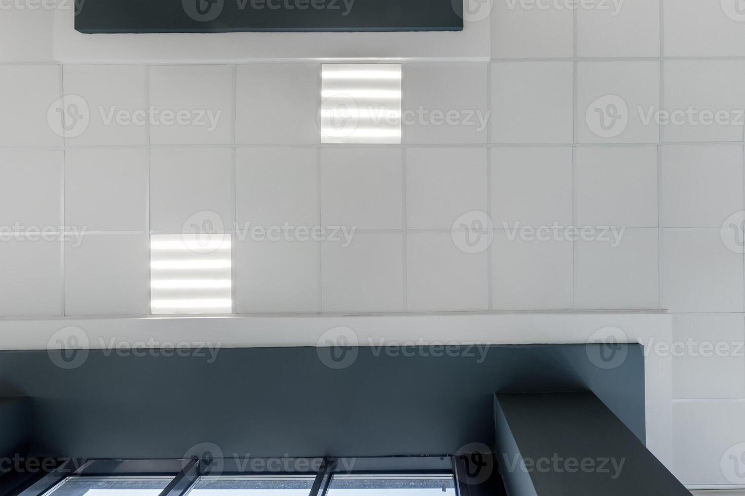 cassette stretched or suspended ceiling with square halogen spots lamps and drywall construction in empty room in house or office with column. Looking up view photo