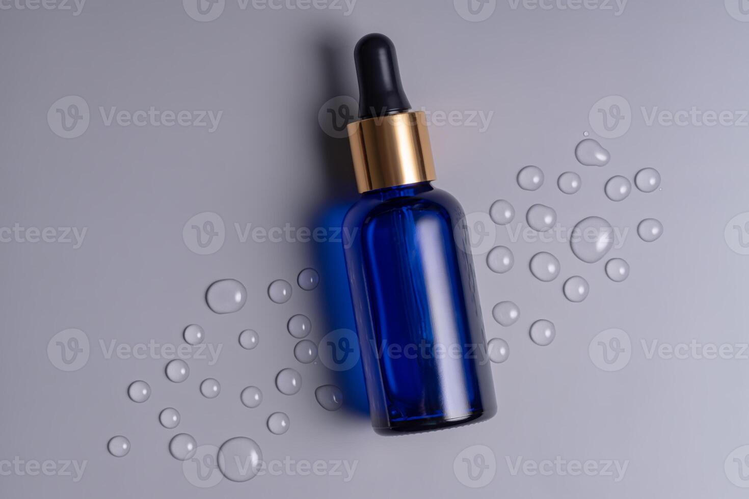 Blank blue glass essential oil bottle with pipette on gray background decorated waterdrops. Skin care concept with natural cosmetics photo