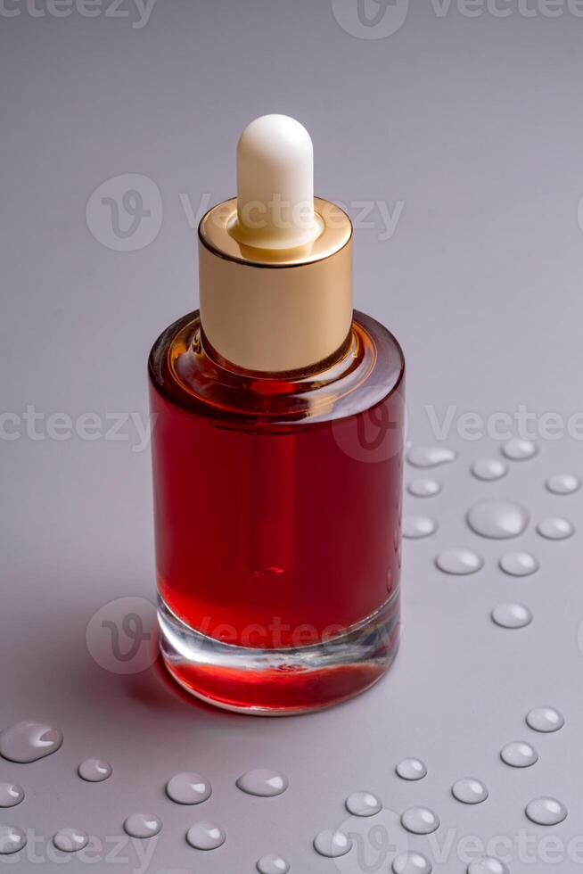 Blank glass essential oil bottle with pipette on gray background decorated water drops. Skin care concept with natural cosmetics photo