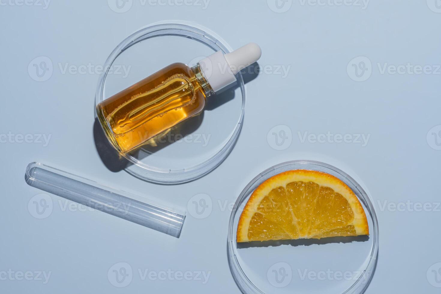 Dropper bottle with orange serum with vitamin C in a petri dish next to orange slice and a test tube. Laboratory cosmetics research, antioxidant testing. Skin care photo
