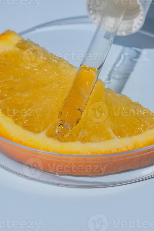 Glass pipette of AHA acid on an orange in glass circle petri dish, blue background. Cosmetics concept photo