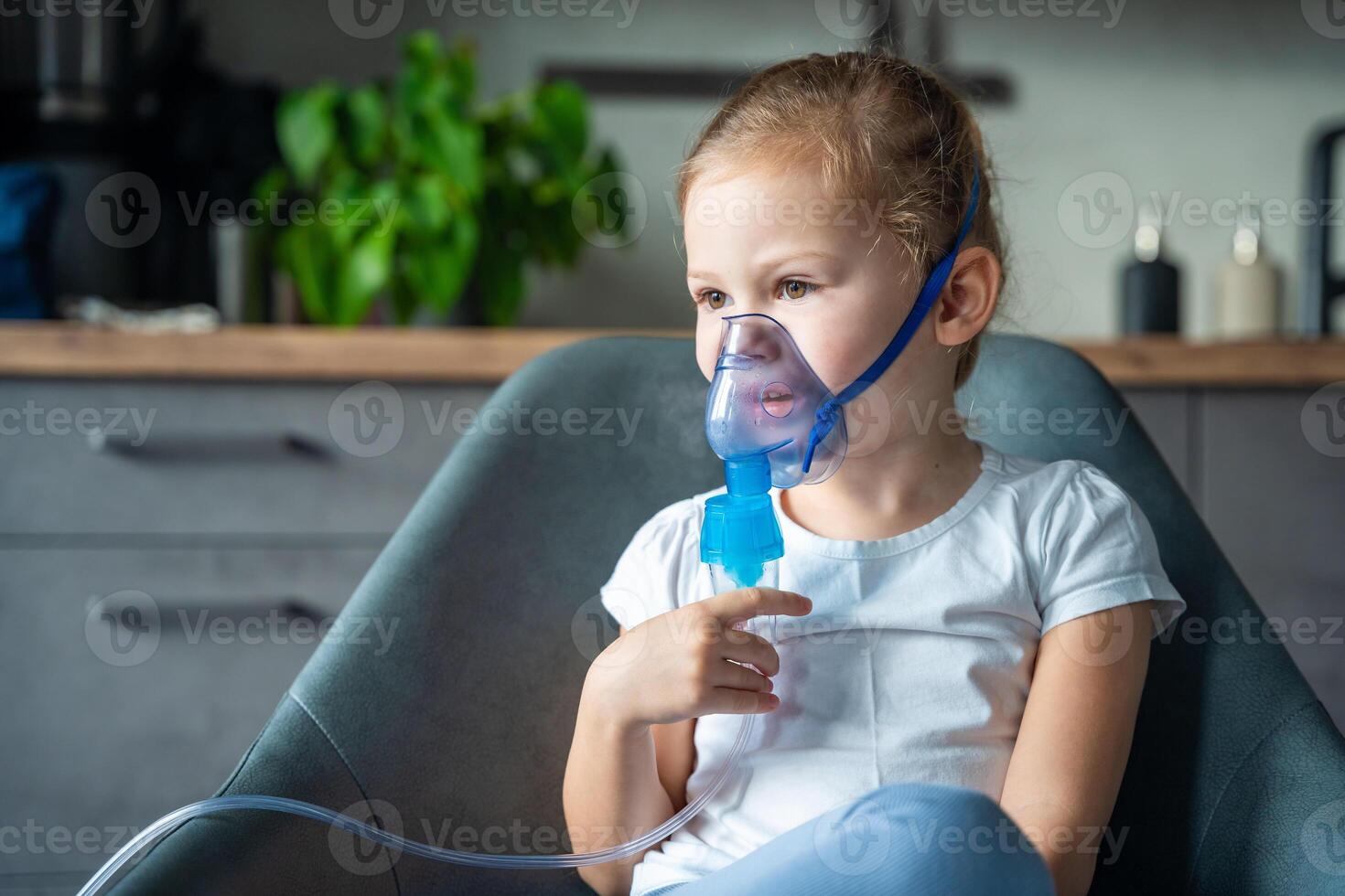 Cute little girl are sitting and holding a nebulizer mask leaning against the face at home on sick leave, airway treatment concept photo