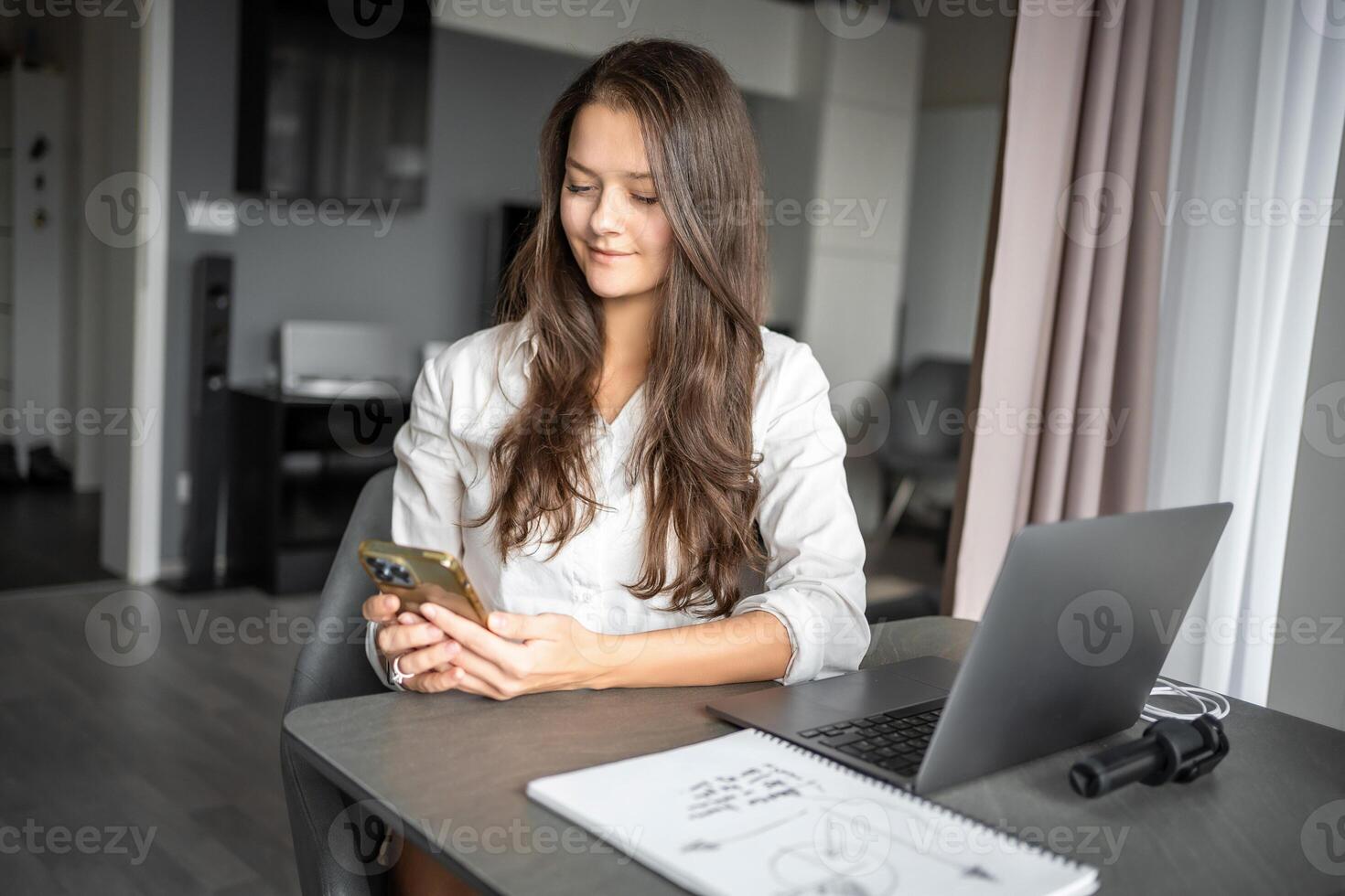 Young woman blogger with smart phone and laptop prepare a content plan using social network in home workplace photo
