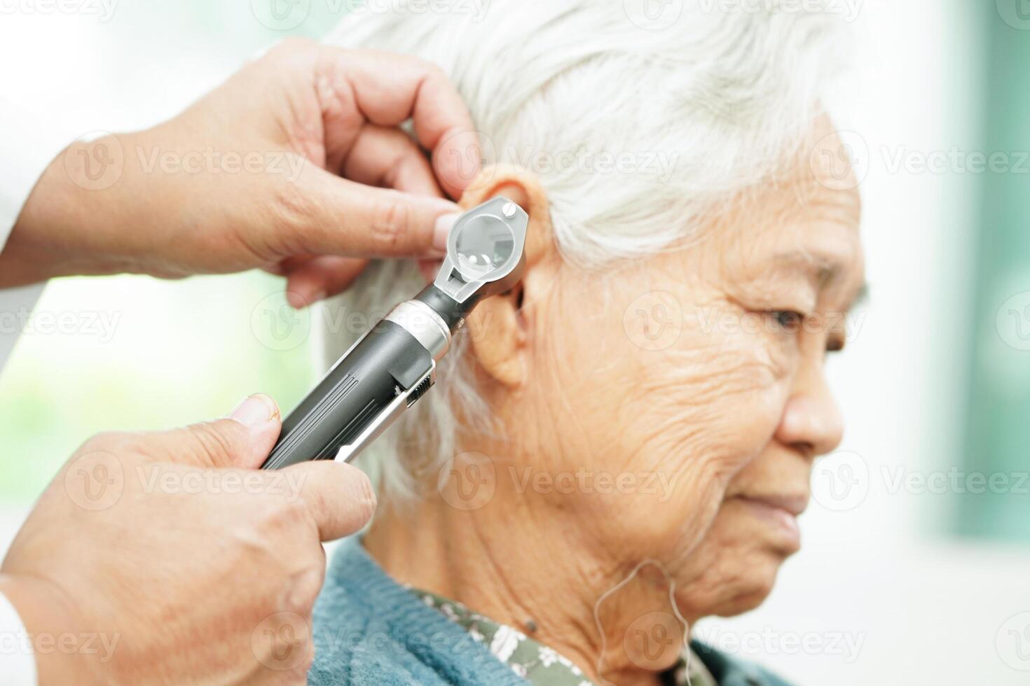 Otolaryngologist or ENT physician doctor examining senior patient ear with otoscope, hearing loss problem. photo